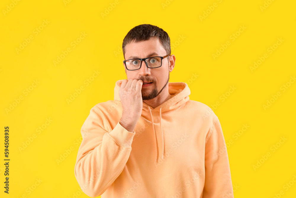 Handsome man in eyeglasses biting nails on yellow background