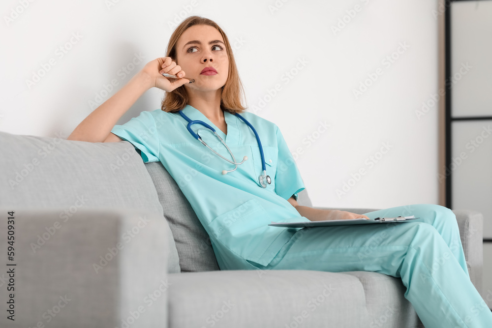 Thoughtful female medical assistant sitting on sofa in modern clinic