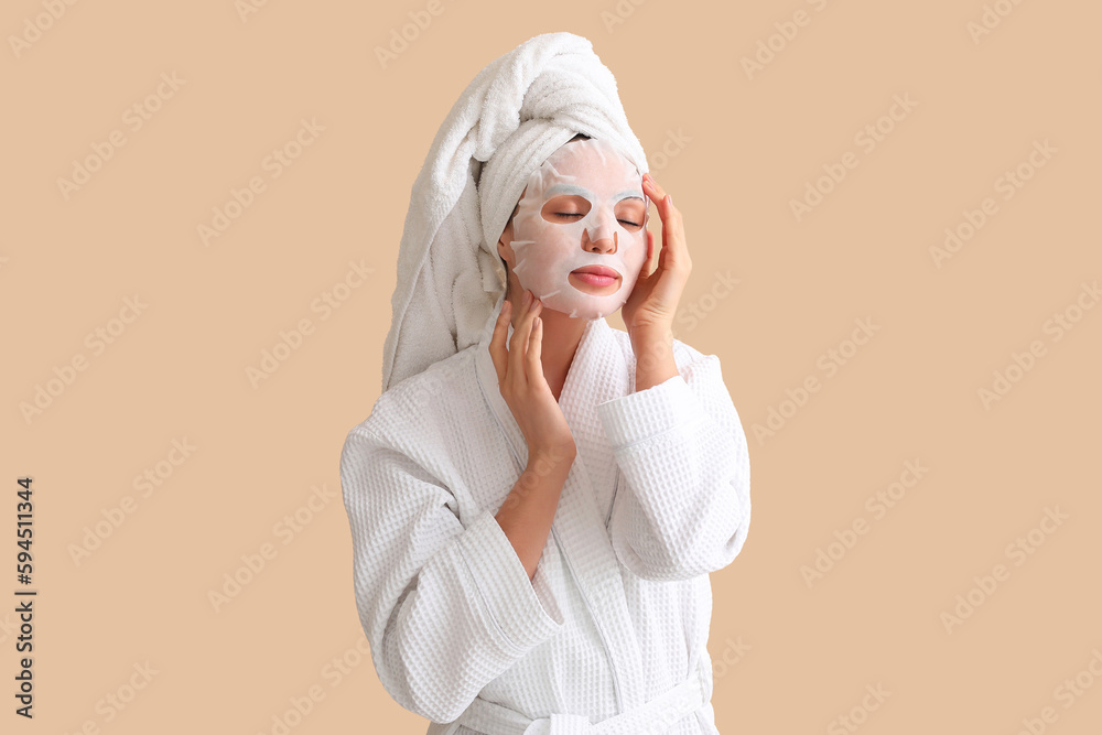 Young woman in bathrobe with sheet mask on beige background