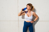 Fototapeta Łazienka - Woman in sportswear drinking water while standing by the wall outdoors