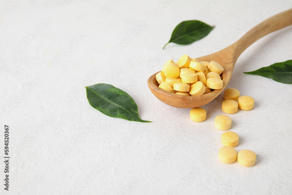 Spoon with pills and leaves on white table, closeup
