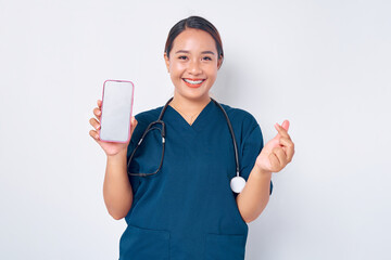 Wall Mural - Happy young Asian woman professional nurse working wearing a blue uniform showing Korean heart love gesture and mobile phone with blank screen isolated on white background. Healthcare medicine concept