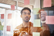 Planning, writing and focused man on glass for project management, workflow and business schedule. Asian person brainstorming ideas, moodboard and sticky notes for solution, reminder or job priority