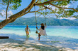 A couple of men and women are on the beach with a rope swing
