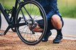 © Azeemud-Deen Jacobs/peopleimages.com - Person, bike and wheel repair outdoor for training, triathlon sports and transportation problem. Closeup of athlete, bicycle and check tire chain for travel safety, cycling maintenance and fixing hub