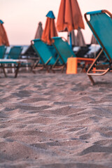 An empty sandy beach by the sea with blue sun loungers and orange umbrellas in the background on a summer evening