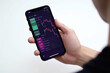 © Iryna - Man holds a phone in his hand with a stock exchange chart. Generative AI