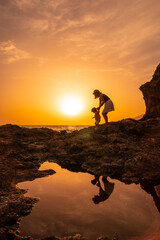 Wall Mural - Silhouette of mother and son walking in the sunset on the beach of Tacoron in El Hierro, Canary Islands, vacation concept, orange sunset, walking by the sea