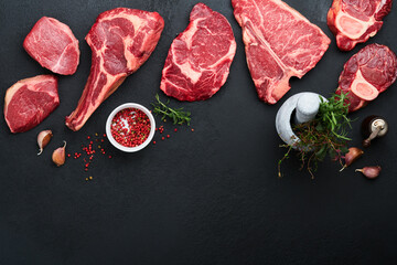 Wall Mural - Raw prime steaks. Variety of fresh black angus prime meat steaks T-bone, New York, Ribeye, Striploin, Tomahawk cutting board on black or dark background. Set of various classic steaks. Top view.