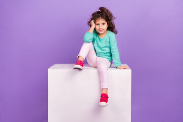 Wall Mural - Photo of adorable sweet little child dressed teal shirt sitting white cube podium empty space isolated violet color background