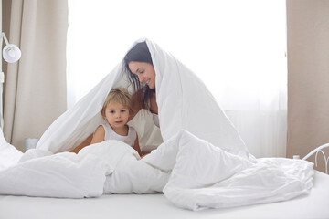 Wall Mural - Beautiful blond child and his mother, playing at home in the morning in bed, smiling, laughing and having fun