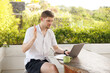 © Girts - Young digital nomad working remotely on his laptop in Bali. Freelancer Man in workation video call. Travel and remote online work. Outdoor in the garden desk for  remote workers someone abroad.