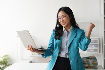 Wall Mural - Young happy business woman worker or feeling excited winning online looking at laptop celebrating professional achievement, getting hired or approved at work