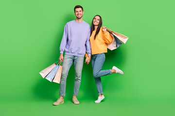 Poster - Full length photo of two lovely partners toothy smile hold hands shop packages isolated on green color background