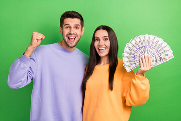 Poster - Photo of two delighted people raise fist celebrate achievement hold dollar banknotes bills isolated on green color background