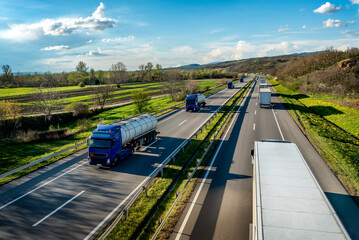 Heavy Highway transportation scene with Convoy of white transportation trucks in one way and blue tank tracks passing in the opposite way on rural highway under a beautiful blue skyv