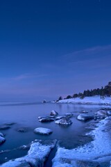 Sticker - Vertical shot of an idyllic frozen rocky shore with blue and pink sunset in the background