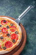 Vertical view of tasty homemade pizza on wooden board on the right side on dark background