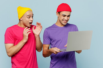 Young amazed happy cool couple two friends IT men wearing casual clothes together hold use work on laptop pc computer show thumb up isolated on pastel plain light blue cyan background studio portrait.