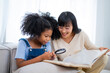© Wanwajee - Asian kind mother teach her daughter using Focus glass on a book to see a tiny thing, relationship between mom and kid concept, mother's day concept.