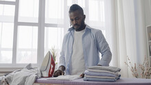 Neat man meticulously folding ironed clothes, doing household chores