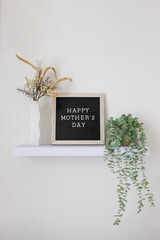 Happy Mother's Day lettering on a black and tan letter board sitting on a floating shelf with plants. modern home decor holiday