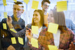 © maxbelchenko - Modern group of people sharing ideas concept with paper note writing strategy in office. Business colleagues write stickers on the glass wall standing in the office. Brainstorming concept.