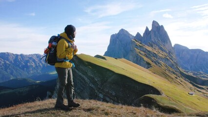 Wall Mural - young man hiking at seceda mountain leaving peak at sunrise. backpack, yellow jacket, boots, beanie.