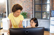 © Wavebreak Media - Two busy diverse female creative colleagues looking at computer and discussing at desk in office