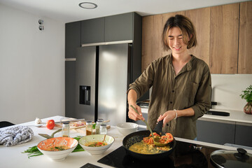 Smiling asian young man cooking chinese or taiwanese tomato scrambled eggs at kitchen.