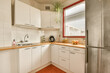 © Casa imágenes - a small kitchen with white cabinets and red trim around the counters, including an orange rug on the floor