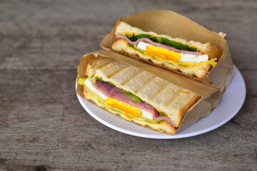 Sandwich cut in half. Two pieces of sandwich with ham, egg, lettuce, tomatoes and sauce in a white plate on old wood table. Top view, copy space