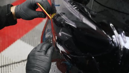 Wall Mural - Close shot of a tinting fil being put with a scraper on a car headlight. High quality 4k footage