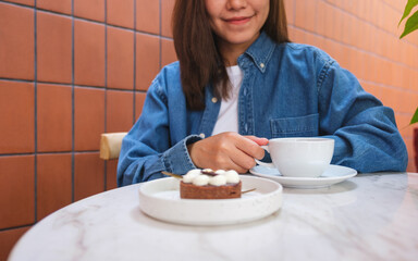 Wall Mural - Closeup image of a young woman drinking coffee and eating a chocolate tart in cafe