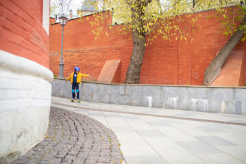 Wall Mural - a boy in a protective helmet rides a yellow city curezer, a plastic skateboard in the spring through the urban streets of the old city	