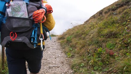 Wall Mural - young man hiker hiking on mountain dirt road with cloudy sky and fog. yellow jacket, backpack, black