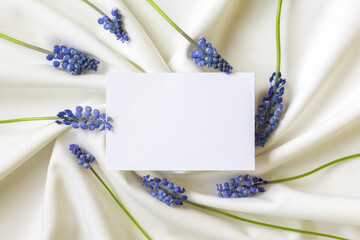 Paper blank in frame of blue spring flowers. Flat lay. Close-up. Copy space for inspirational texts, beautiful quotes or positive sayings.