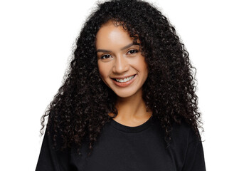 optimistic curly young woman with gentle smile, looks positively at camera, wears casual black cloth