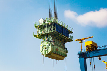 Transportation of a large marine engine by a port crane using steel cables.