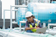 © amorn - Female engineer worker using laptop computer inspecting quality sewer pipes at rooftop of building. African American woman engineer working, checking or maintenance sewer pipes at construction site