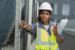 © amorn - Female engineer worker working, holding blueprint and inspecting structure of building at rooftop of building at construction site
