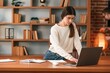 © standret - Young woman in glasses is working indoors. Standing by table with laptop