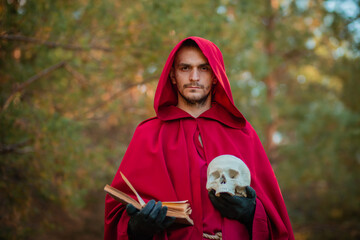 Wall Mural - A sorcerer in red clothes with a skull and a book in his hands reads a spell. Medieval monk reads a prayer.