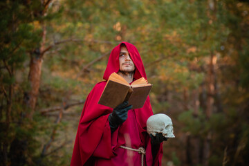 Wall Mural - A sorcerer in red clothes with a skull and a book in his hands reads a spell. Medieval monk reads a prayer.