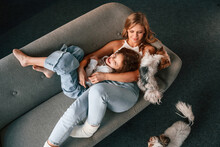 Positive Emotions, Relaxing On The Sofa. Mother With Her Daughter And With Two Cute Dogs Is In Domestic Room