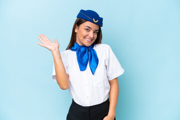 Poster - Airplane stewardess caucasian woman isolated on blue background saluting with hand with happy expression