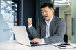© Liubomir - Successful asian investor financier celebrating victory and triumph, mature boss in business suit working inside office with laptop, man received online win news.