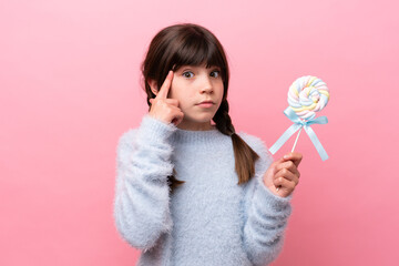 Wall Mural - Little caucasian girl holding a lollipop thinking an idea