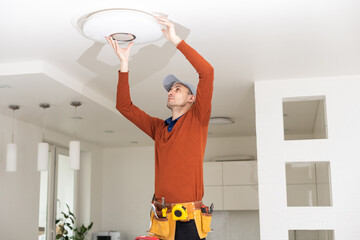 Electrician in uniform repairing ceiling lamp indoors