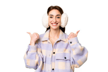 Wall Mural - Young caucasian woman wearing winter muffs over isolated chroma key background with thumbs up gesture and smiling